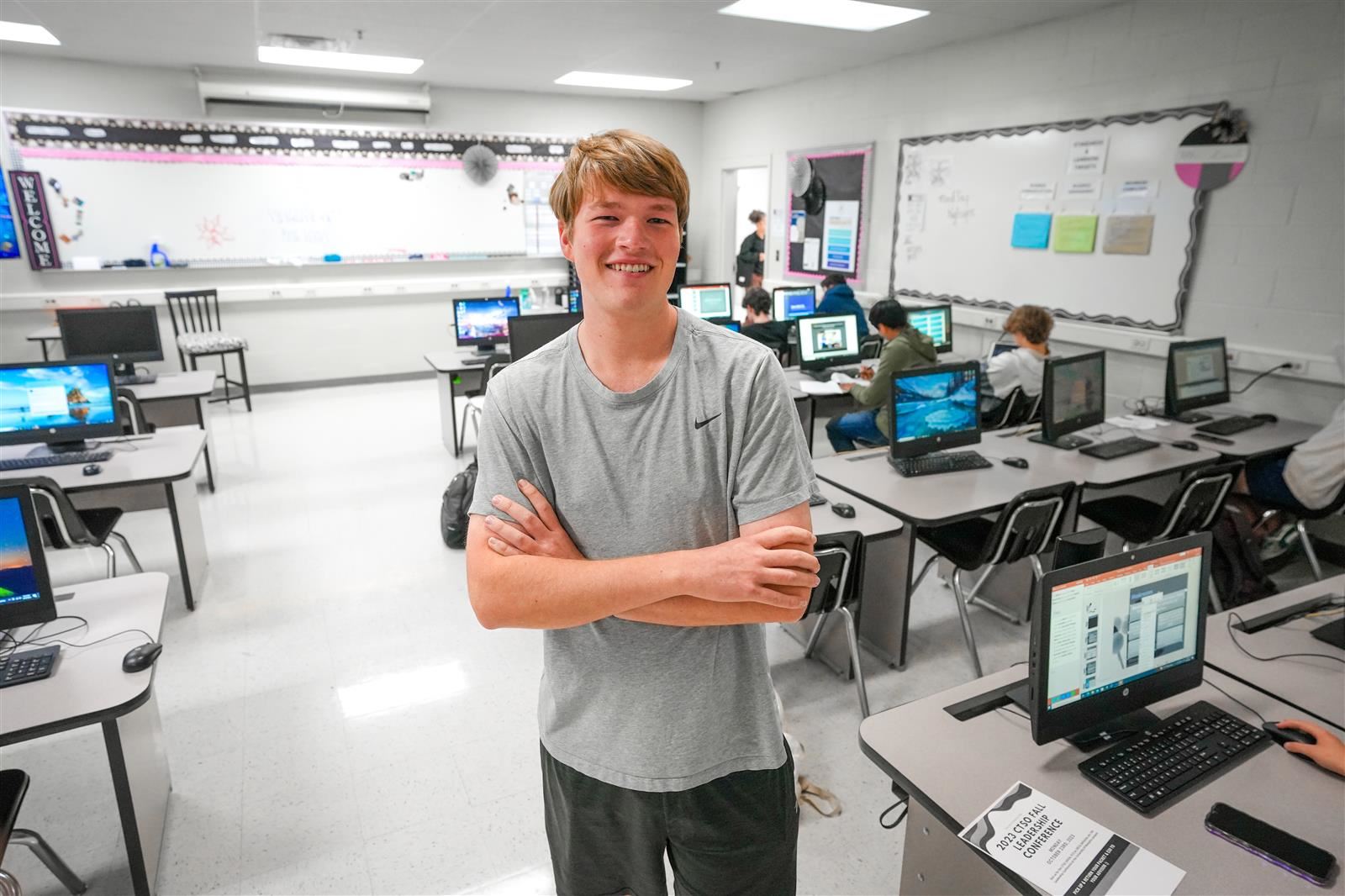 a young man stands in a computer lab crossing his arms